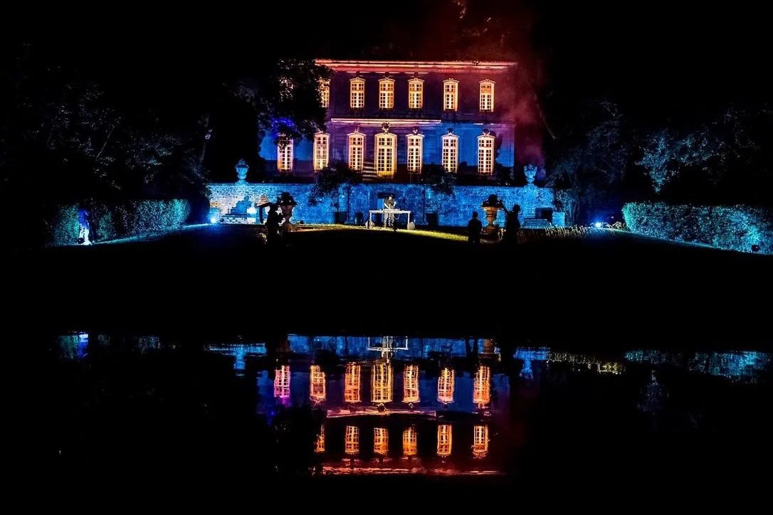 Façade d'une demeure illuminée en bleu et ambre, reflet dans le bassin