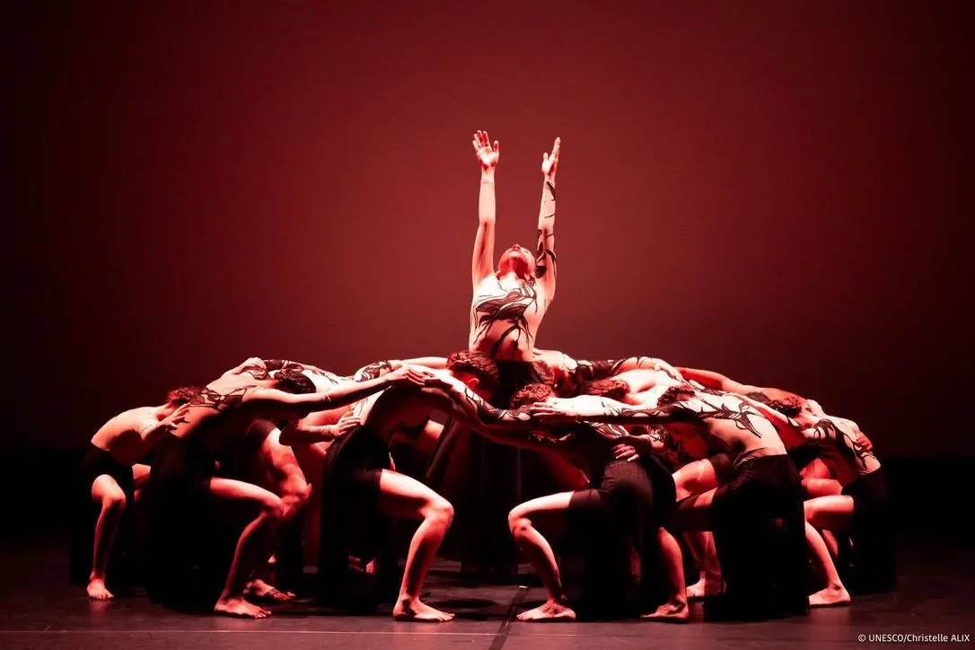 Danseuses en cercle sous une lumière rouge, bras levés vers le ciel